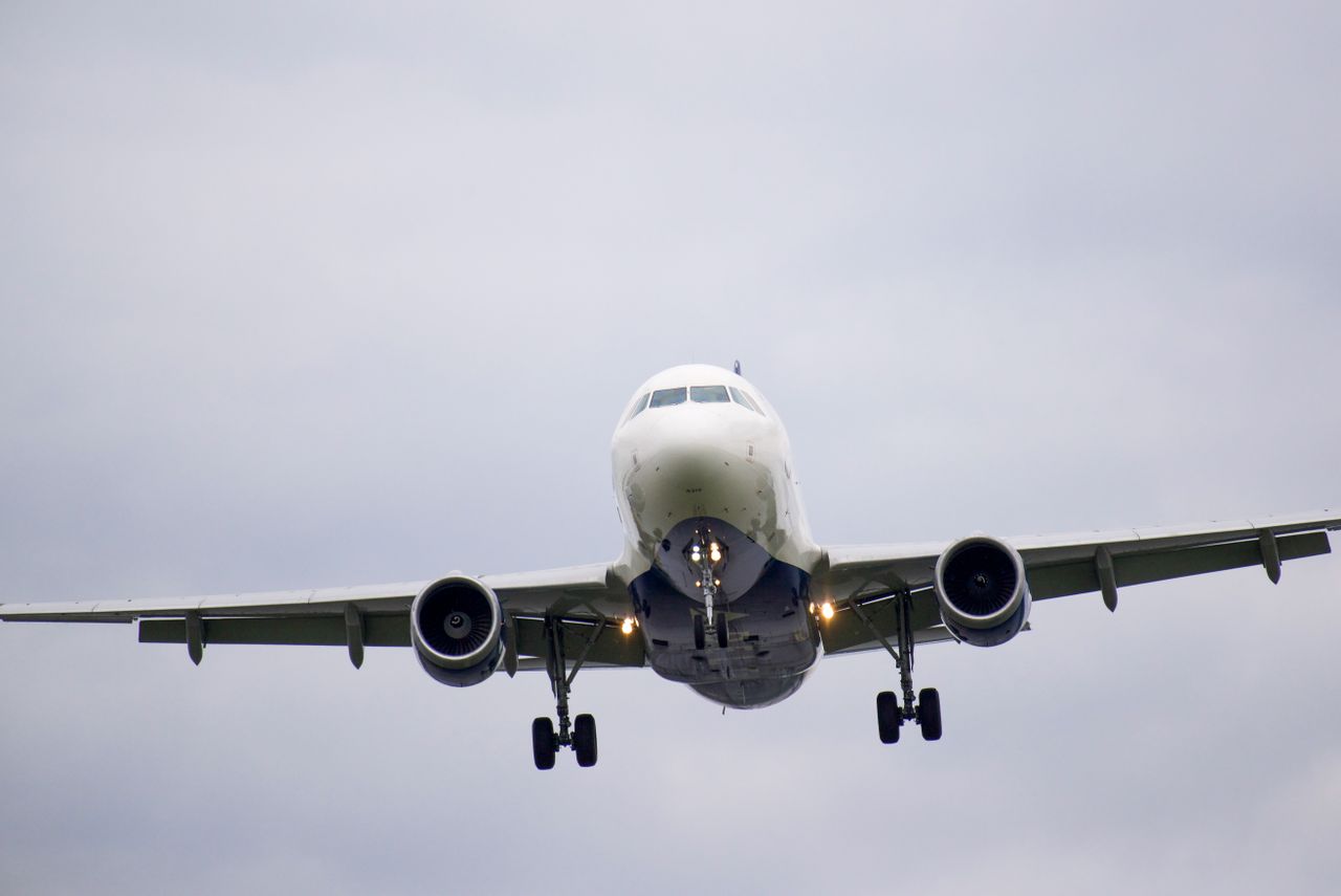 A commercial airplane approaching for landing against a cloudy sky backdrop.