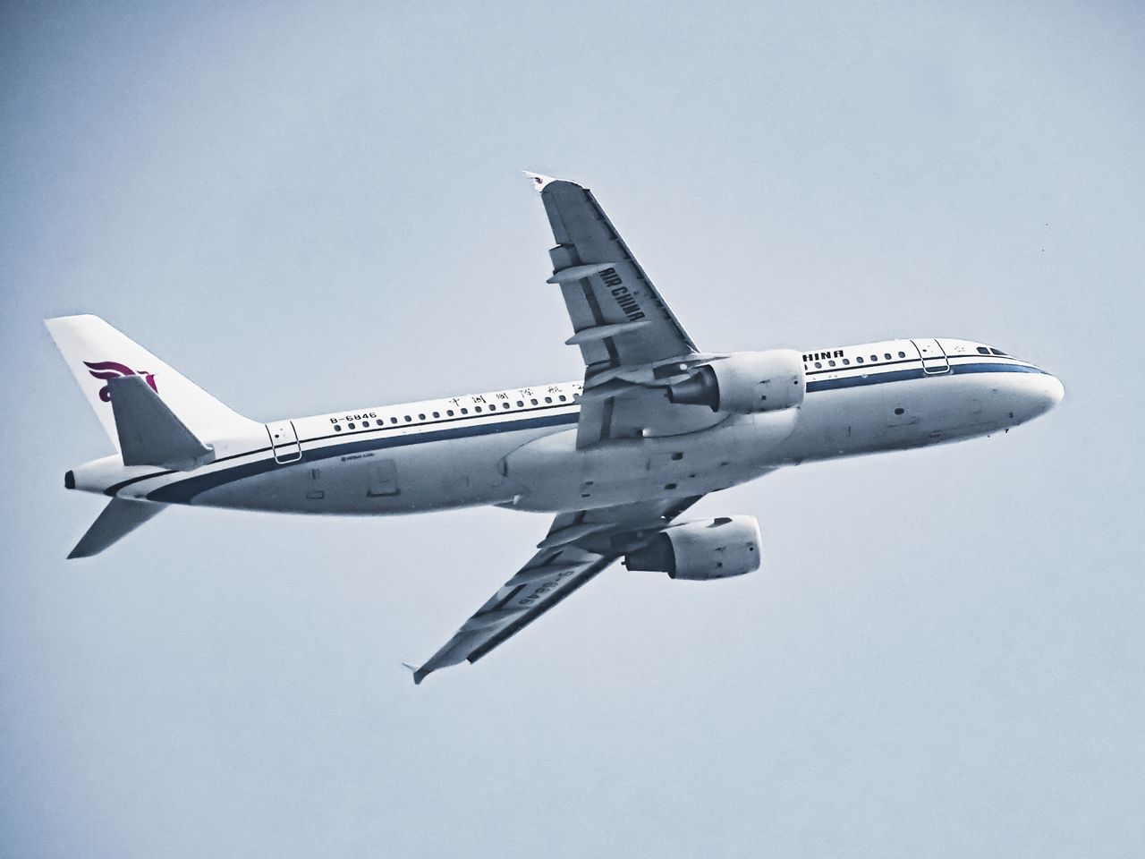 An Air China airplane in flight against a pale blue sky, showcasing aviation and travel.