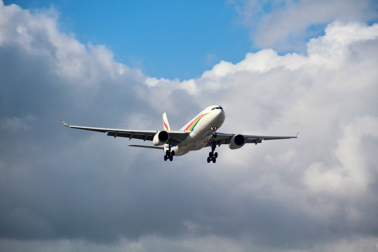 A commercial airline jet soaring through the sky with large clouds in the background.