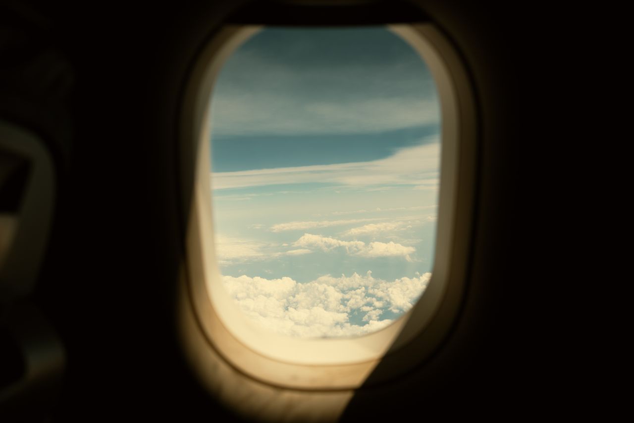 Scenic aerial view of clouds and blue sky through an airplane window, capturing the essence of air travel.